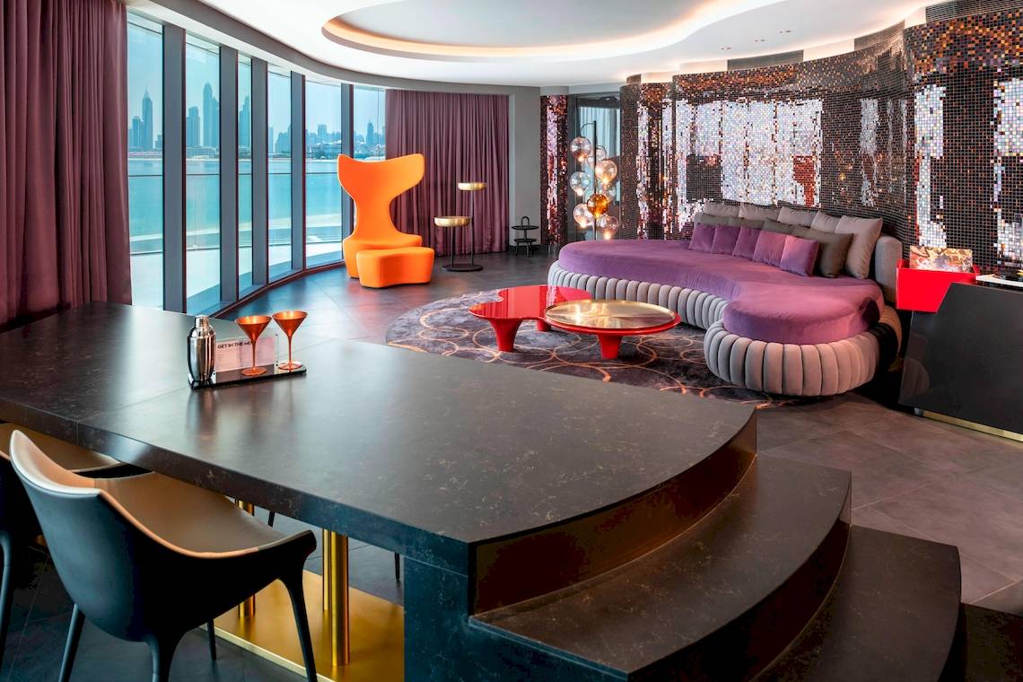 Innenansicht der Suite im W Dubai - The Palm mit großem Fenster, modernem Möbelstück und Blick auf die Stadt.