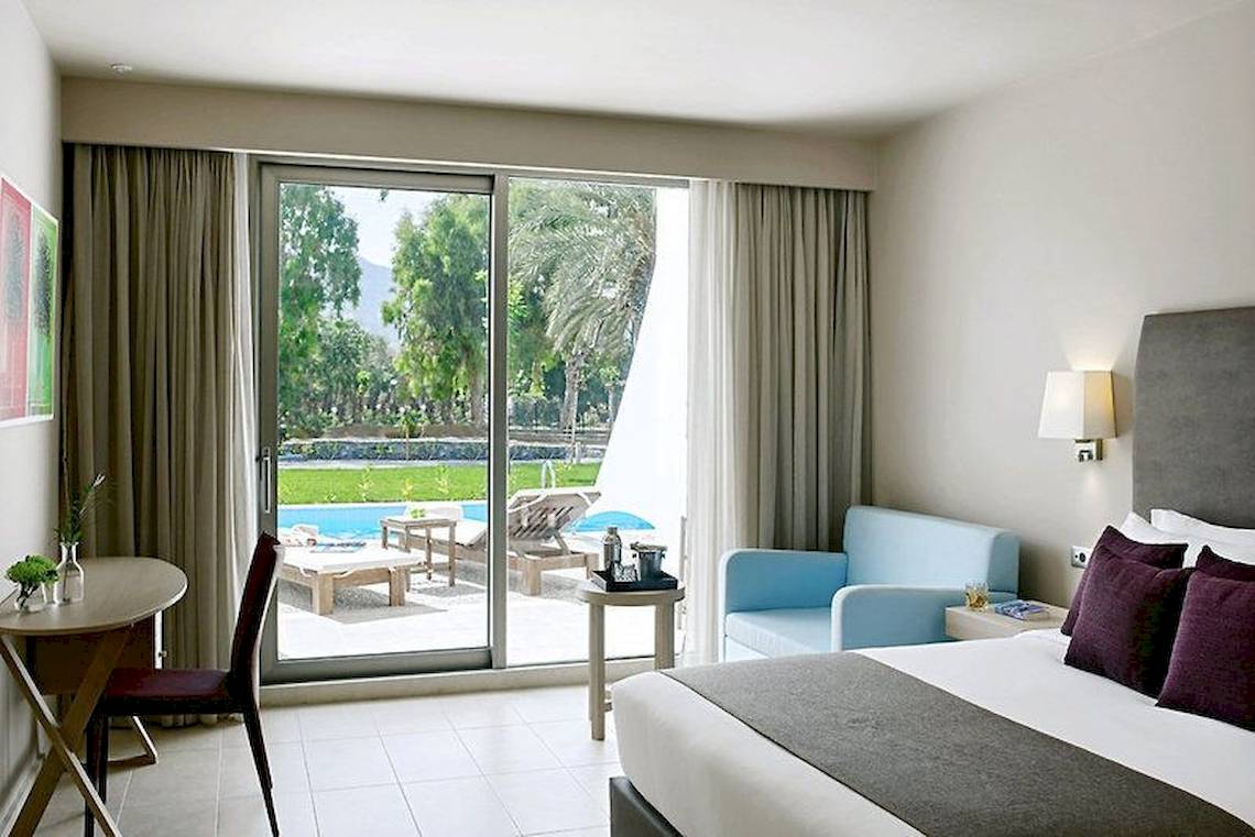 Zimmer im Atlantica Akti Zeus Hotel mit großer Glastür und Poolblick.