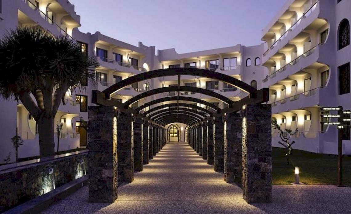 Beleuchteter Eingang des Atlantica Akti Zeus Hotels mit Arkaden und Gehweg.