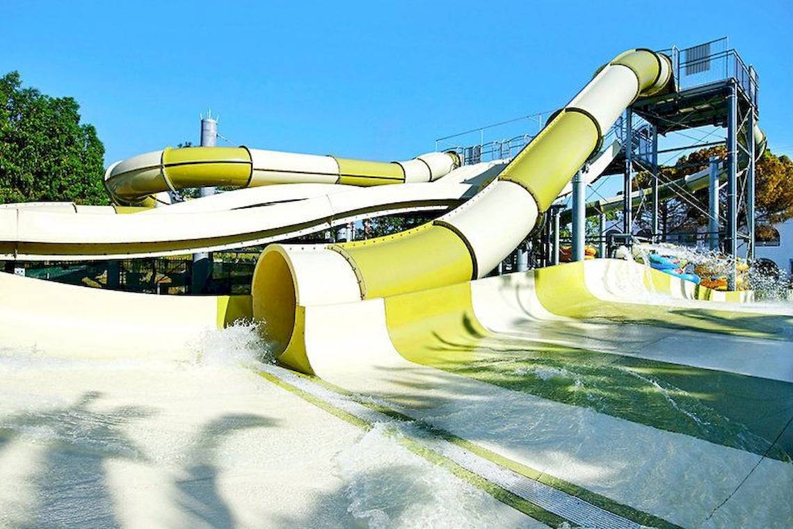 Wasserrutsche im Freizeitpark Atlantica Akti Zeus mit Wasser und Bäumen im Hintergrund.