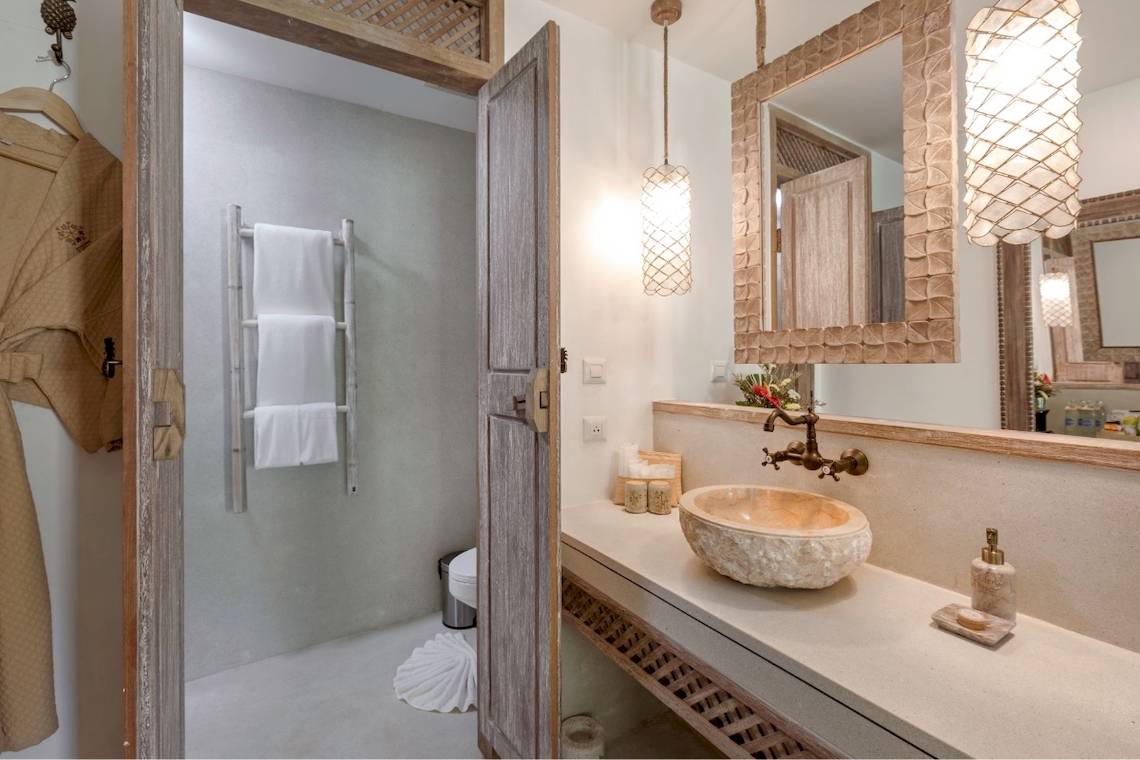 Badezimmer im Eden Beach Khao Lak Resort & Spa mit einer offenen Tür, einem Waschbecken und einem Spiegel.