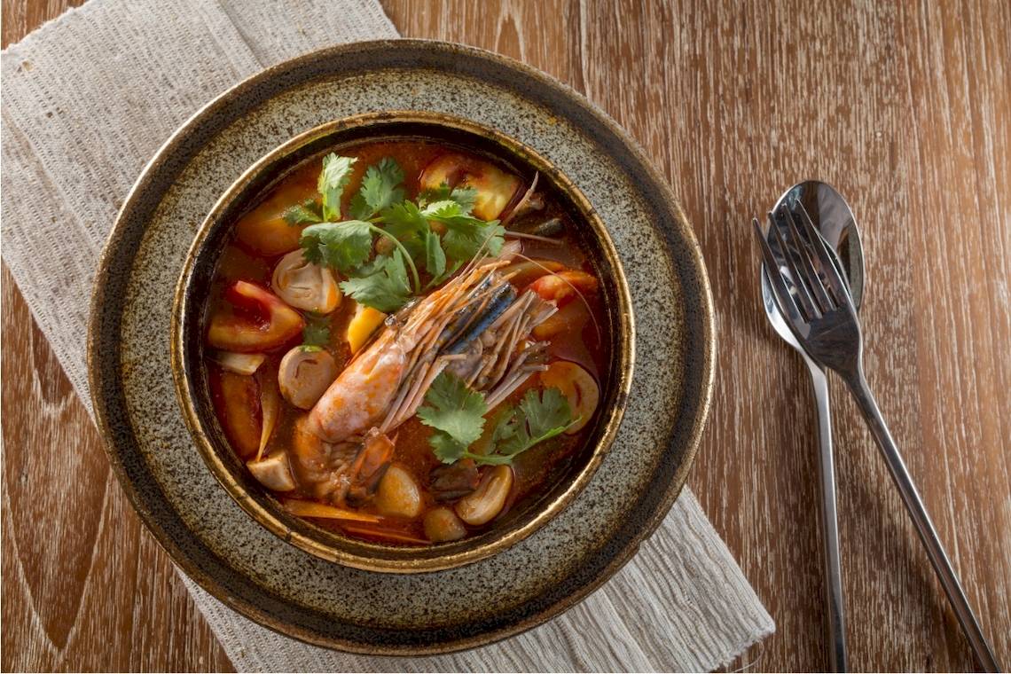 Suedost-asiatische Suppe in einem Bowl auf einem Holztisch mit einem Loffel und einer Gabel