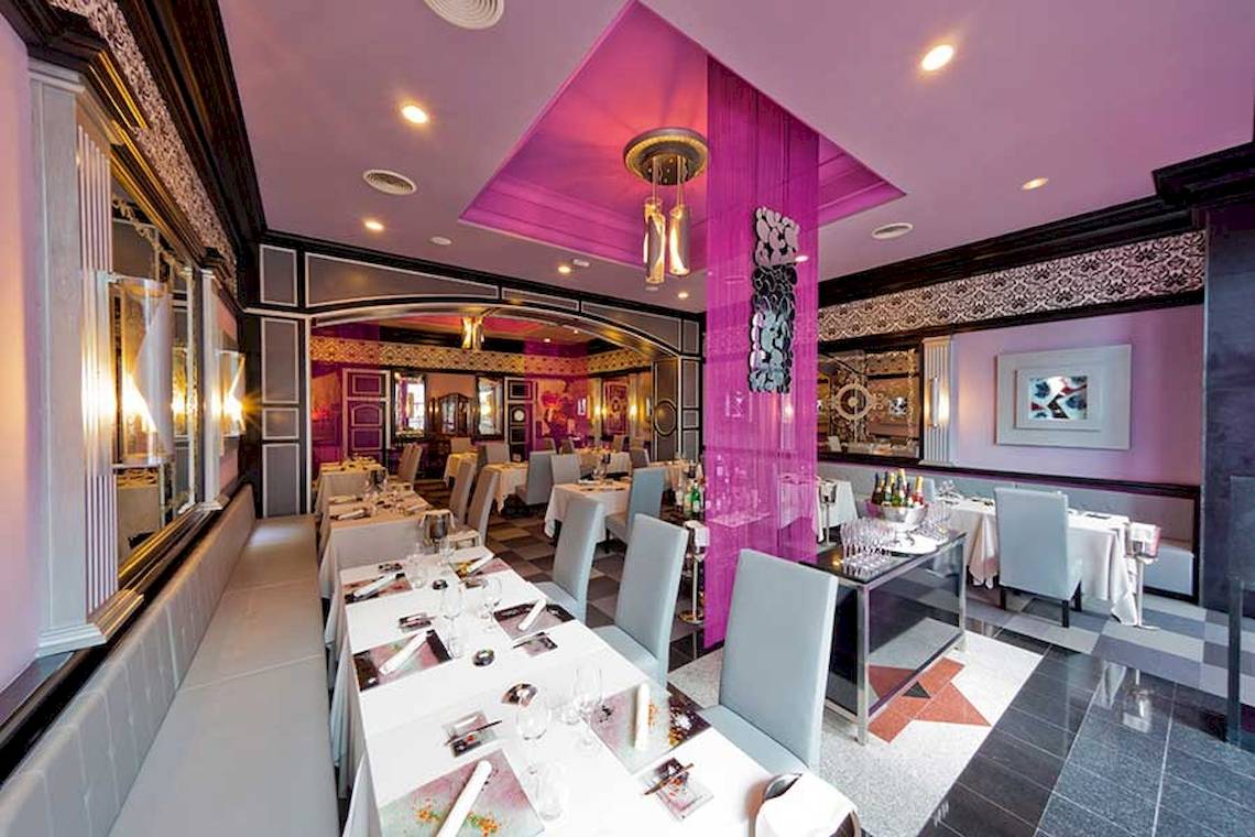 Innenraum des Restaurants im Riu Palace Las Americas mit Tisch, Stühlen und lila Wänden.