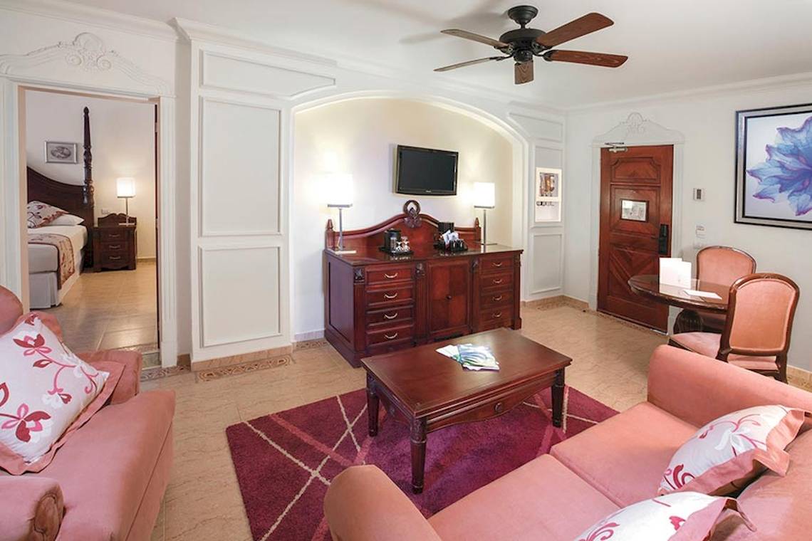 Innenraum des Riu Palace Las Americas Hotels mit Wohnzimmer, Fernseher, Couch, Tisch und Esstisch