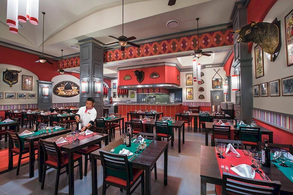 Restaurant im Riu Palace Las Americas mit roter Einrichtung und einem Kellner, der eine Flasche öffnet.