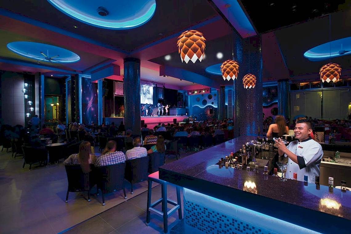 Bar im Riu Palace Las Americas bei Nacht mit einem Barkeeper, der einen Cocktail mixt.