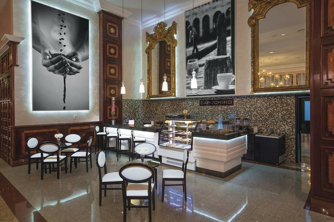 Innenansicht des Cafés im Riu Palace Las Americas Hotel mit Sitzgelegenheiten und einer Theke.