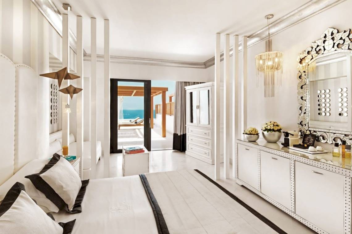 Schlafzimmer im Mitsis Alila Resort & Spa mit Meerblick, weißen Möbeln und modernen Dekorationen.