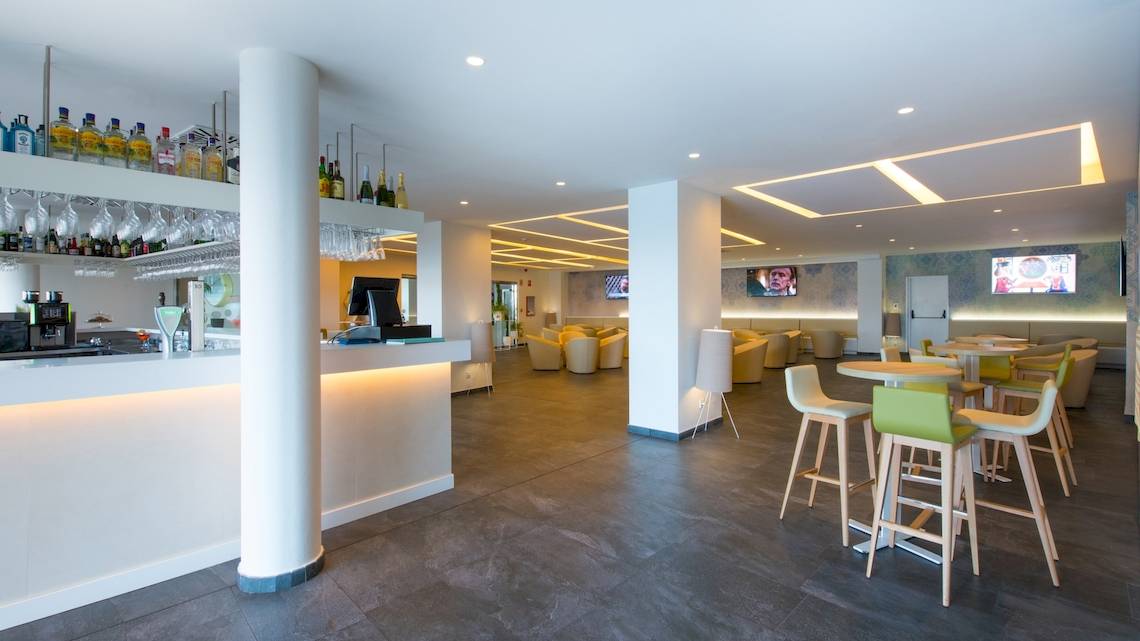 Innenansicht der Bar im Iberostar Selection Lanzarote Park Hotel mit gepolsterten Stühlen und Tischen, einer Theke und Fernsehern an der Wand.
