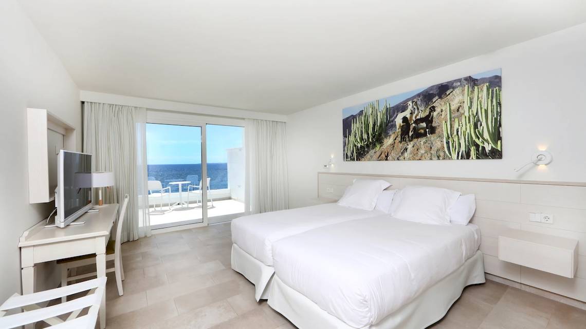 Ein modernes Hotelzimmer mit zwei Betten, Blick auf das Meer und eine Terrasse.
