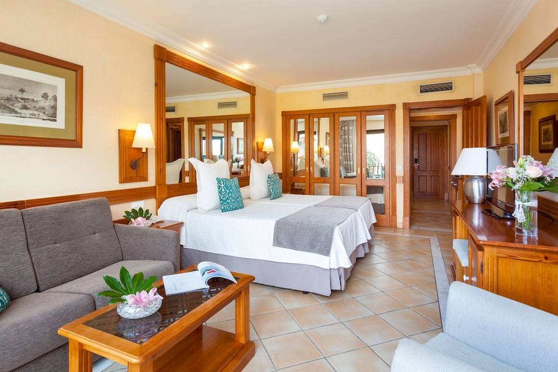 Hotelzimmer im GF Gran Costa Adeje mit zwei Betten, Sofa, Tisch und Blumenvase