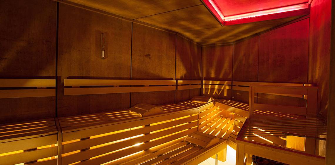 Innenansicht der Sauna im Lopesan Villa del Conde Resort & Thalasso mit Holzbänken und roter Beleuchtung.
