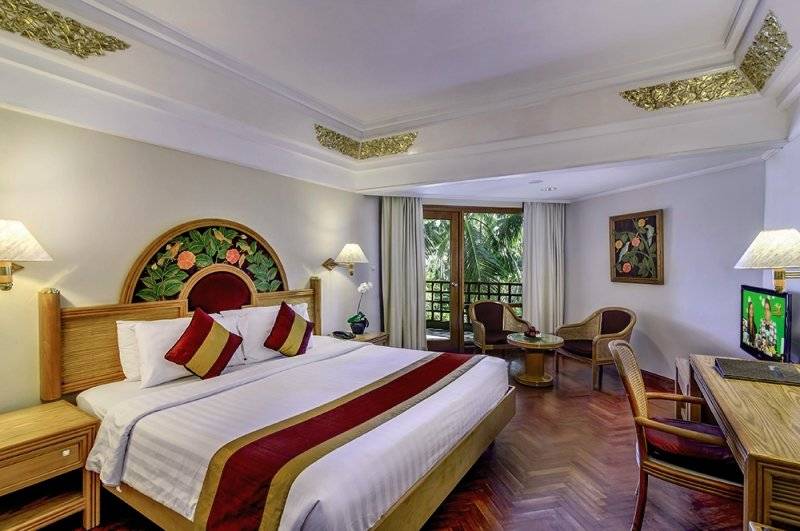 Innenansicht eines Hotelzimmers im Prama Sanur Beach Bali, mit Bett, Schreibtisch und Fernseher.