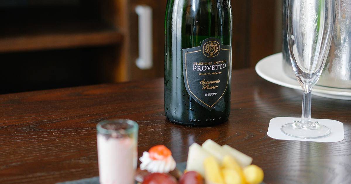Eine Flasche Provento Spumante Bianco Brut neben einem Glas und kleinen Happen auf einem Tisch.