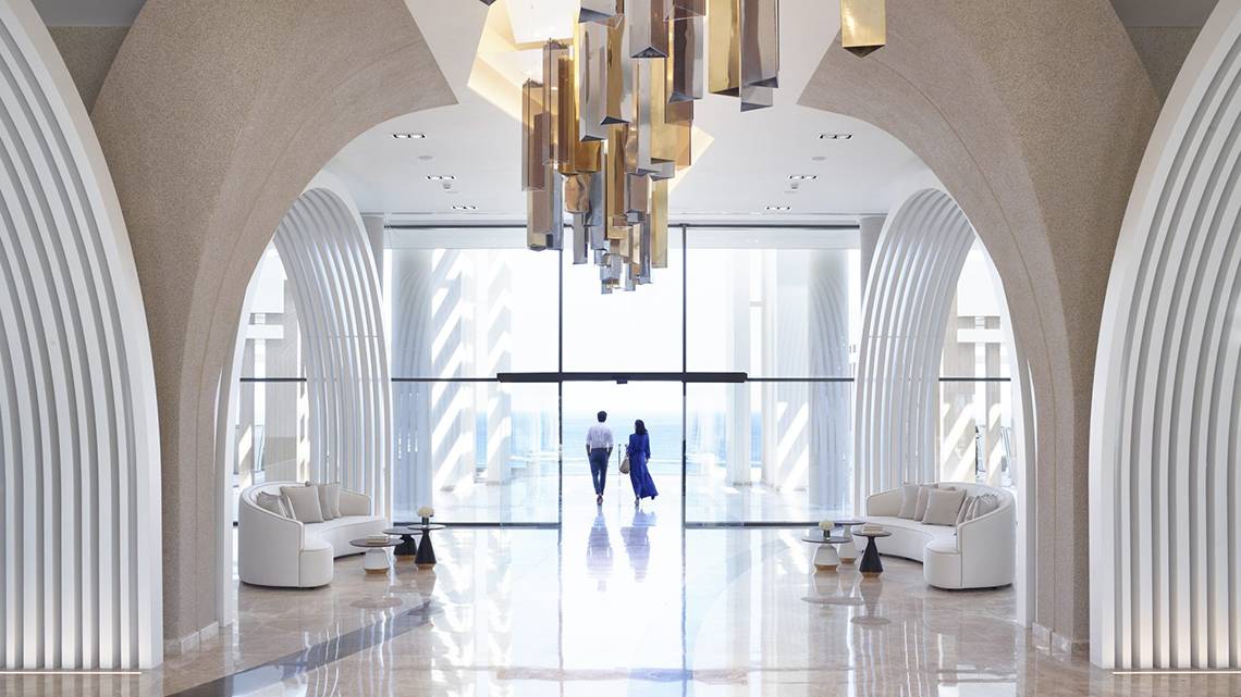 Innenansicht der Lobby des Mayia Exclusive Resort & Spa mit zwei Personen, die durch eine geräumige Eingangshalle gehen.