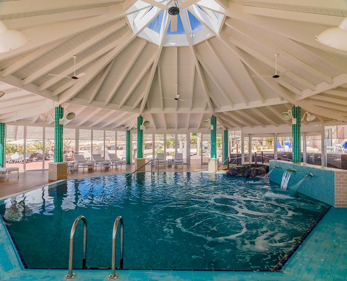 Innenbereich des Poolbereichs im H10 Playa Esmeralda Hotel mit Glasdach und grünen Säulen