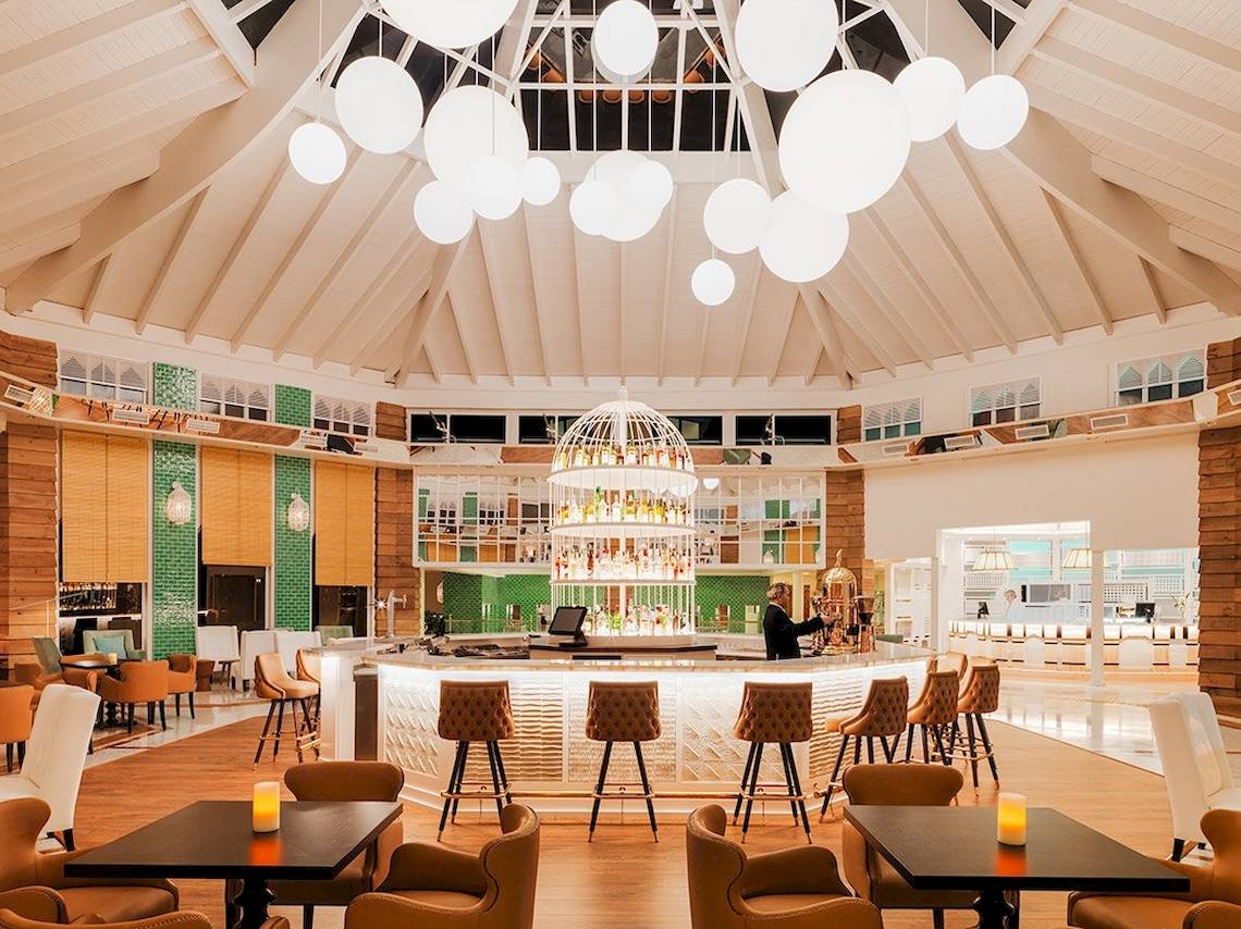 Lobby-Bar im H10 Playa Esmeralda Hotel mit einer Person hinter der Theke, umgeben von Holztischen und Stühlen.