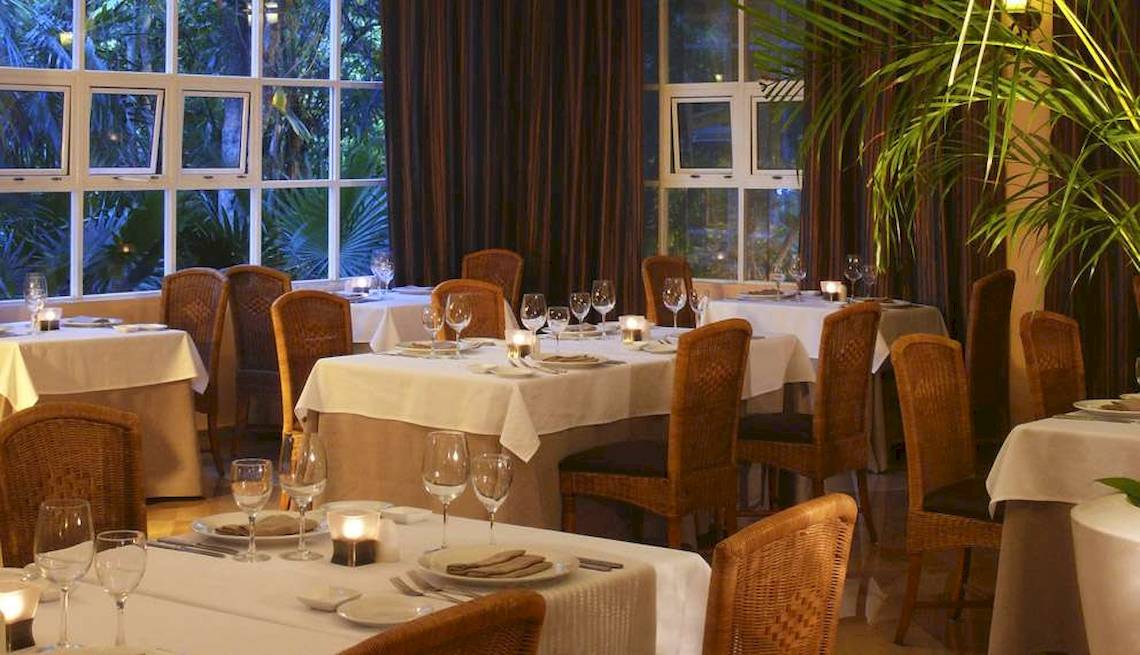 Innenansicht des Restaurants im Catalonia Royal Tulum Hotel mit gedeckten Tischen und Blick auf den Garten