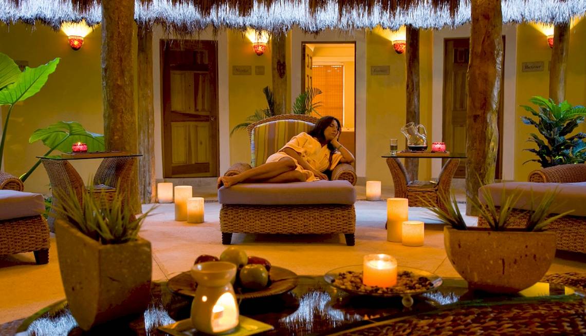 Eine Frau entspannt sich im Wellnessbereich des Hotels Catalonia Royal Tulum, umgeben von Kerzen und Pflanzen.