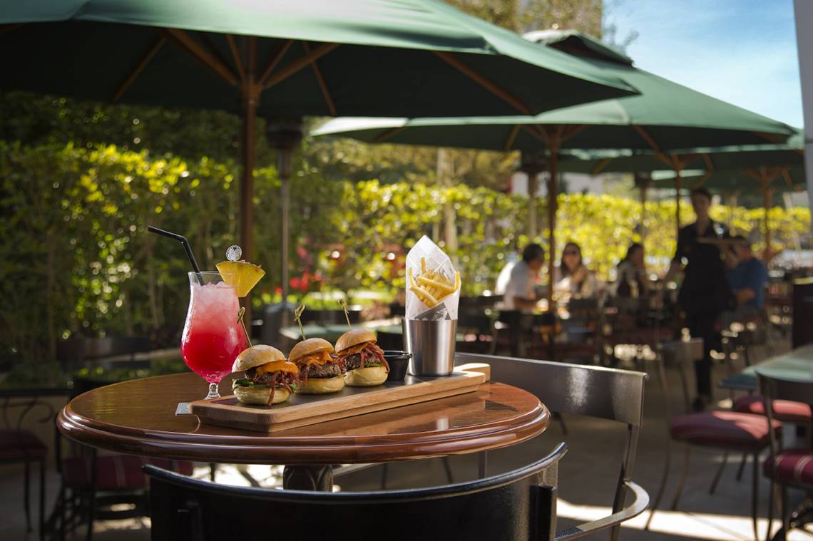 Terrasse im Park Rotana Abu Dhabi mit Burgern, Pommes und Getränken.