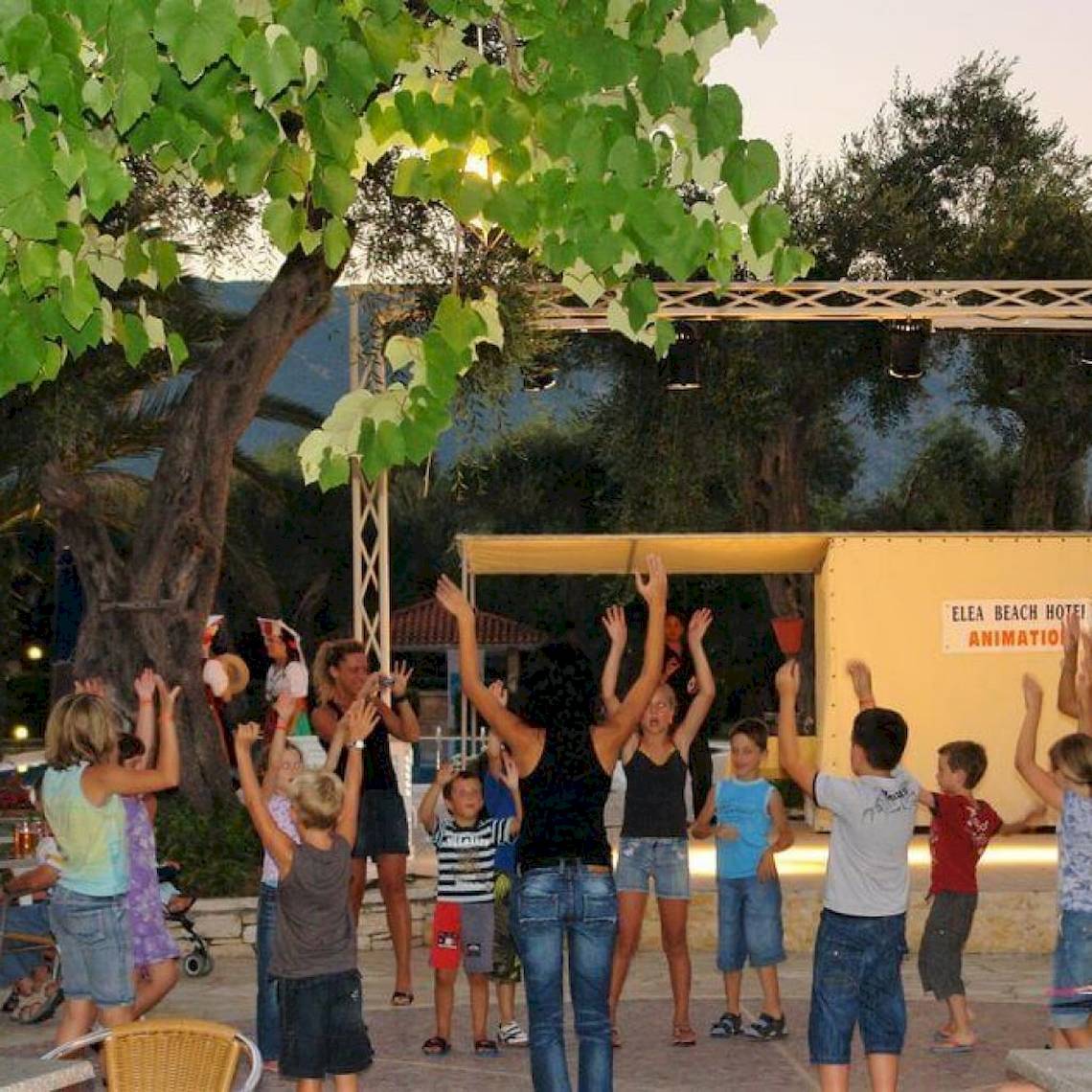 Animation vor dem Elea Beach Hotel mit Kindern und Erwachsenen, die die Hände in die Luft strecken.