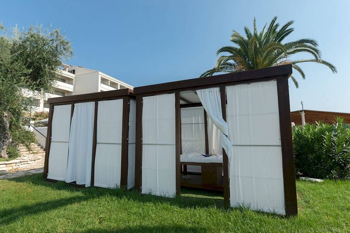 Schlafzelt im Garten des Elea Beach Hotels mit weißem Vorhang und Palme im Hintergrund.