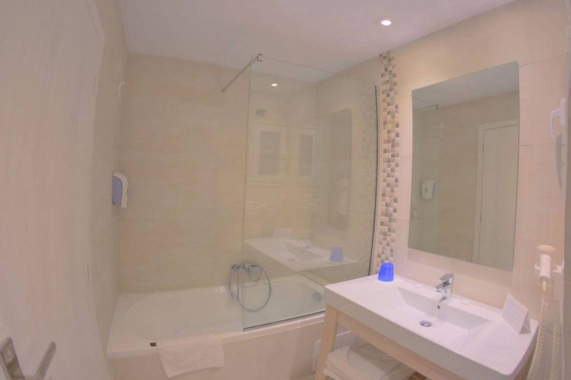 Badezimmer im Elea Beach Hotel mit Badewanne, Dusche, Waschbecken und Spiegel.