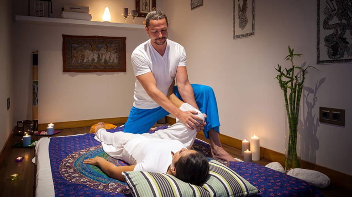 Mann führt Massage an einer Frau in einem Hotelzimmer durch, beide tragen weiße Kleidung.