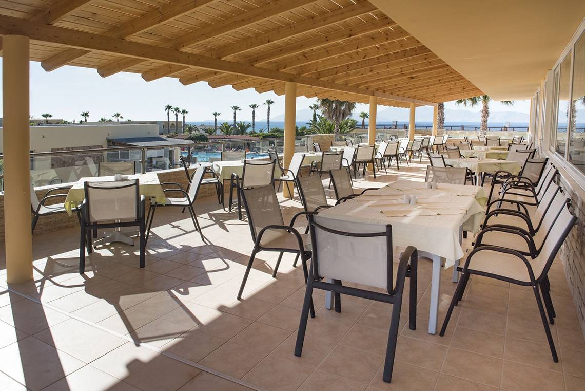 Terrasse des Eurovillage Achilleas Hotels mit Tischen und Stühlen und Blick auf das Meer.