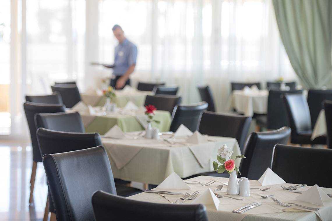 Gedeckter Tisch im Speisesaal des Eurovillage Achilleas Hotels mit Kellner im Hintergrund.