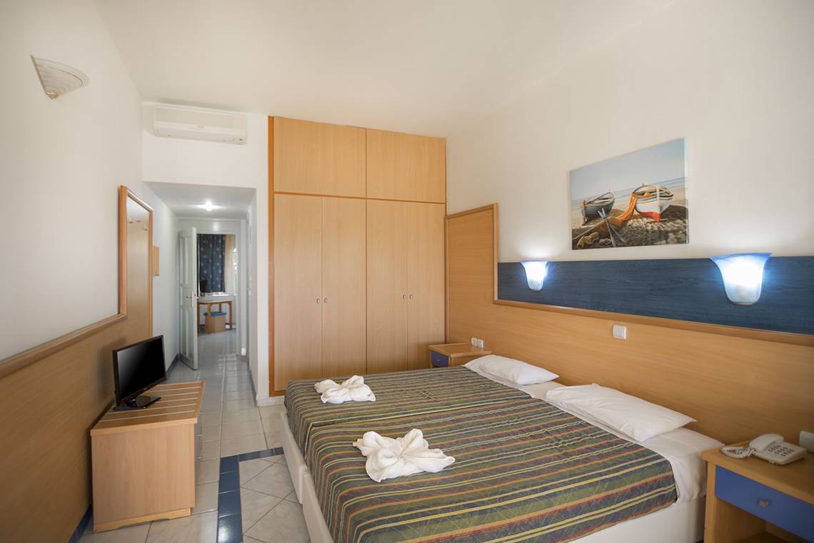 Innenansicht eines Hotelzimmers im Eurovillage Achilleas mit zwei Betten, Fernseher, Kleiderschrank und Deko.