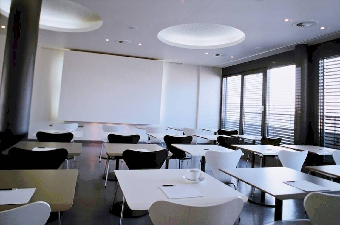 Konferenzraum im Ku Damm 101 Hotel mit weißen Tischen und Stühlen, einer Kaffeetasse und Notizblöcken.