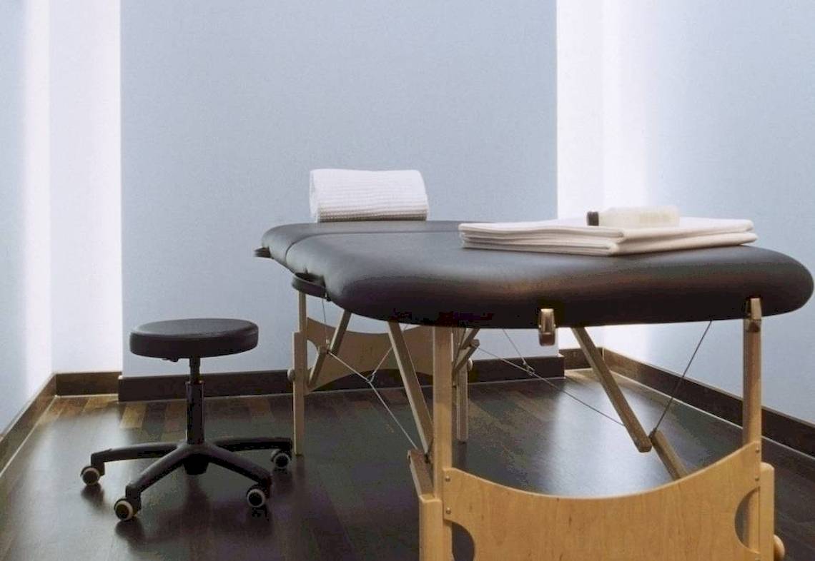 Massage-Behandlungsraum im Hotel Ku Damm 101 mit schwarzem Tisch und weißem Stuhl.