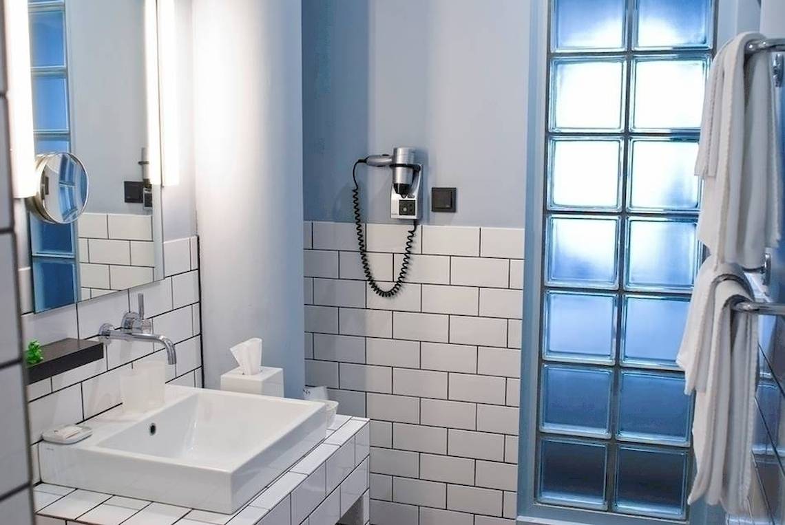 Badezimmer im Ku Damm 101 Hotel mit weißem Waschbecken, Spiegel und blauen Fliesen.