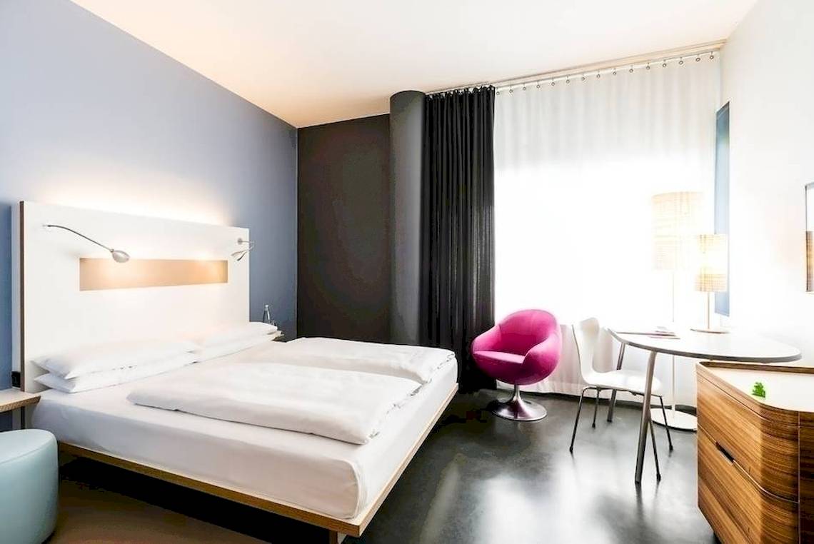 Innenansicht eines modernen Hotelzimmers im Ku Damm 101 mit zwei Betten, einem Schreibtisch und Stühlen.