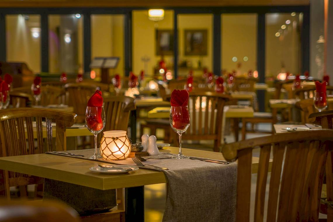 Restauranttisch im Le Peninsula Bay Beach Resort mit rotem Weinglas und Kerze.
