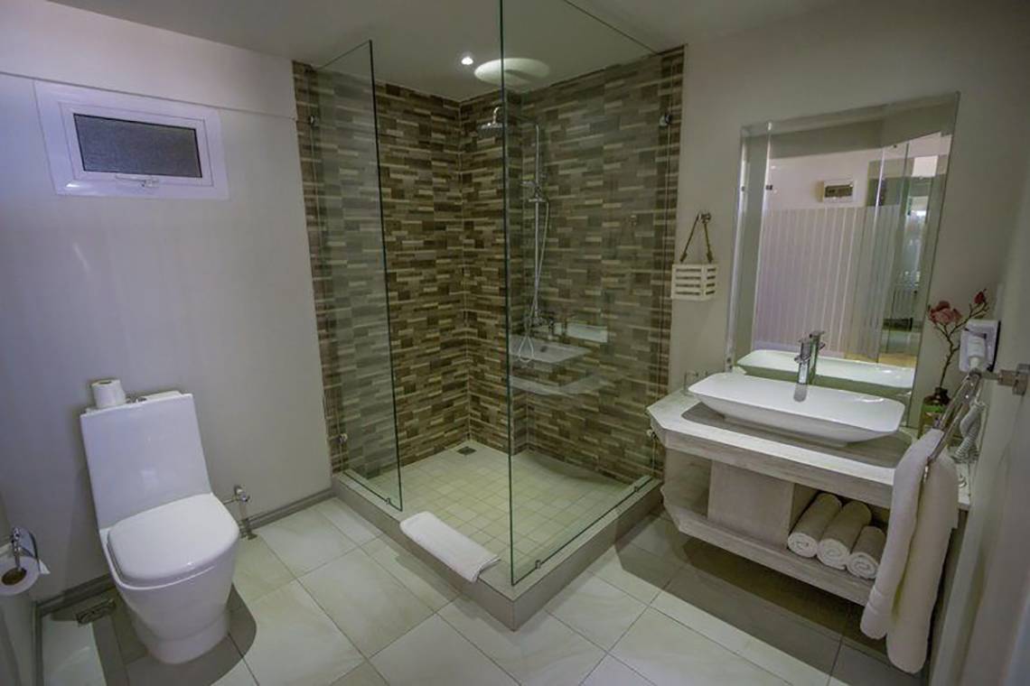 Badezimmer im Le Peninsula Bay Beach Resort & Spa mit Glasdusche, Toilette, Waschbecken und Spiegel.
