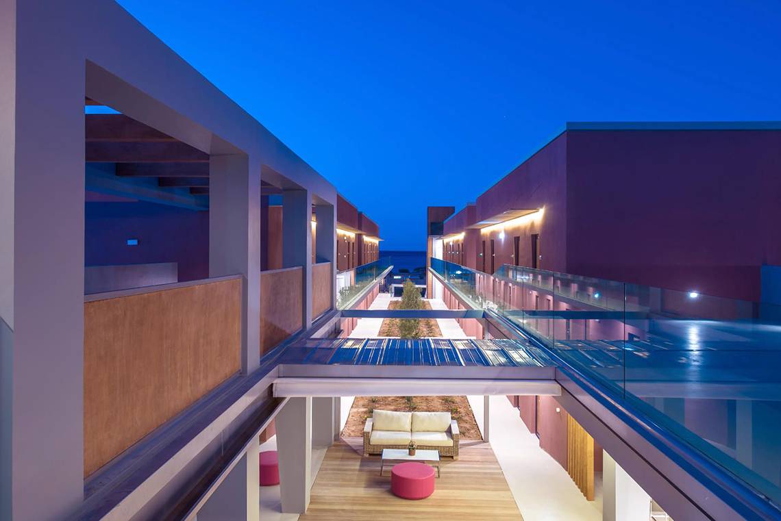 Innenbereich des Corissia Princess Hotels bei Nacht mit einer Glasbrücke und Möbeln.