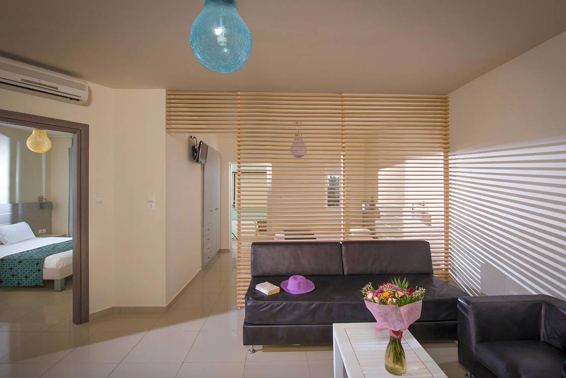 Wohnbereich des Corissia Princess Hotels mit Couch, Tisch und Bett im Hintergrund.