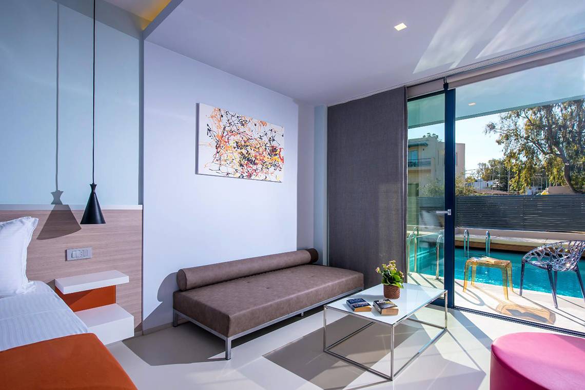 Innenansicht eines Zimmers im Corissia Princess Hotel mit Bett, Sofa, Tisch und Poolzugang.