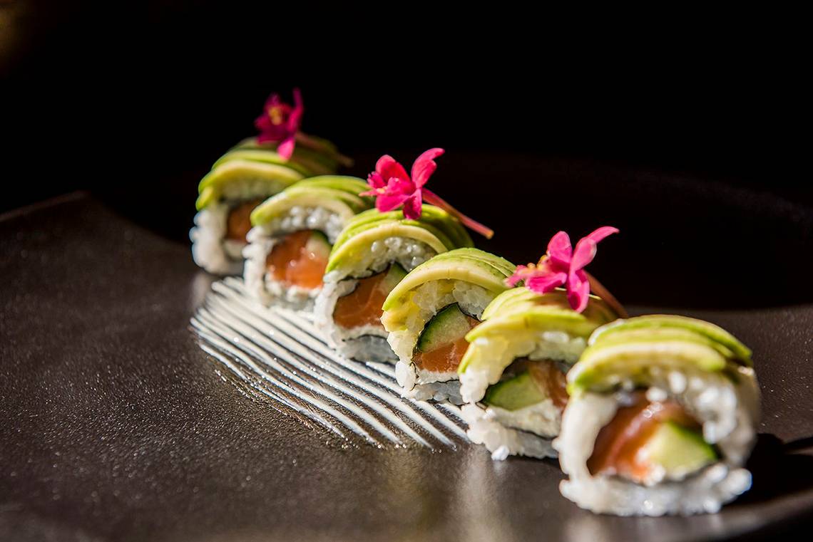 Foto von mehreren Sushi-Rollen mit Avocado und Lachs auf einem schwarzen Teller.