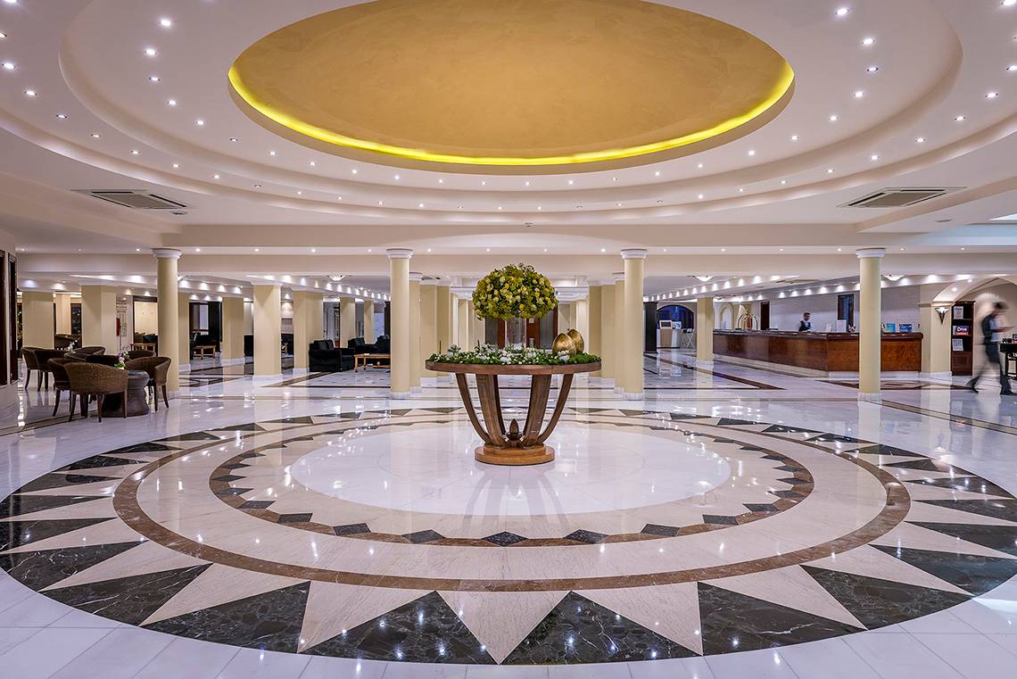 Die geräumige Lobby des Mitsis Grand Hotel Beach mit einer zentralen Blumeninstallation und gemustertem Boden.