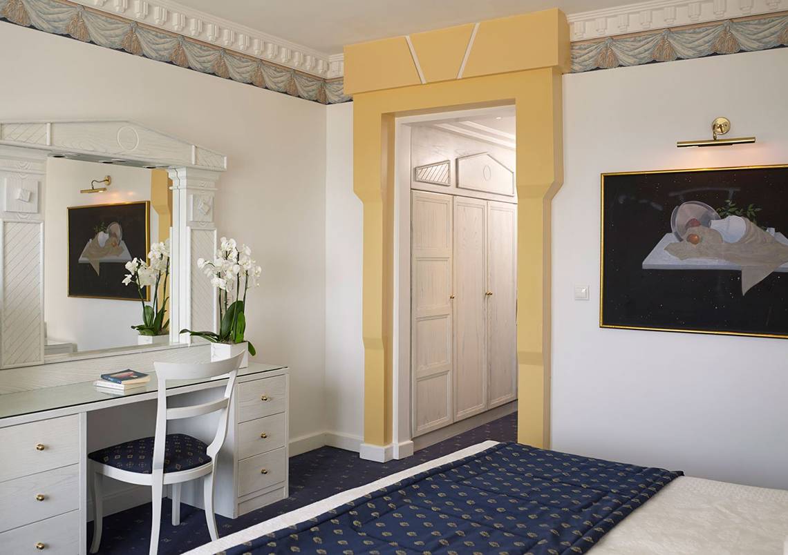 Innenansicht eines Zimmers im Mitsis Grand Hotel Beach mit Bett, Schreibtisch und Spiegel.