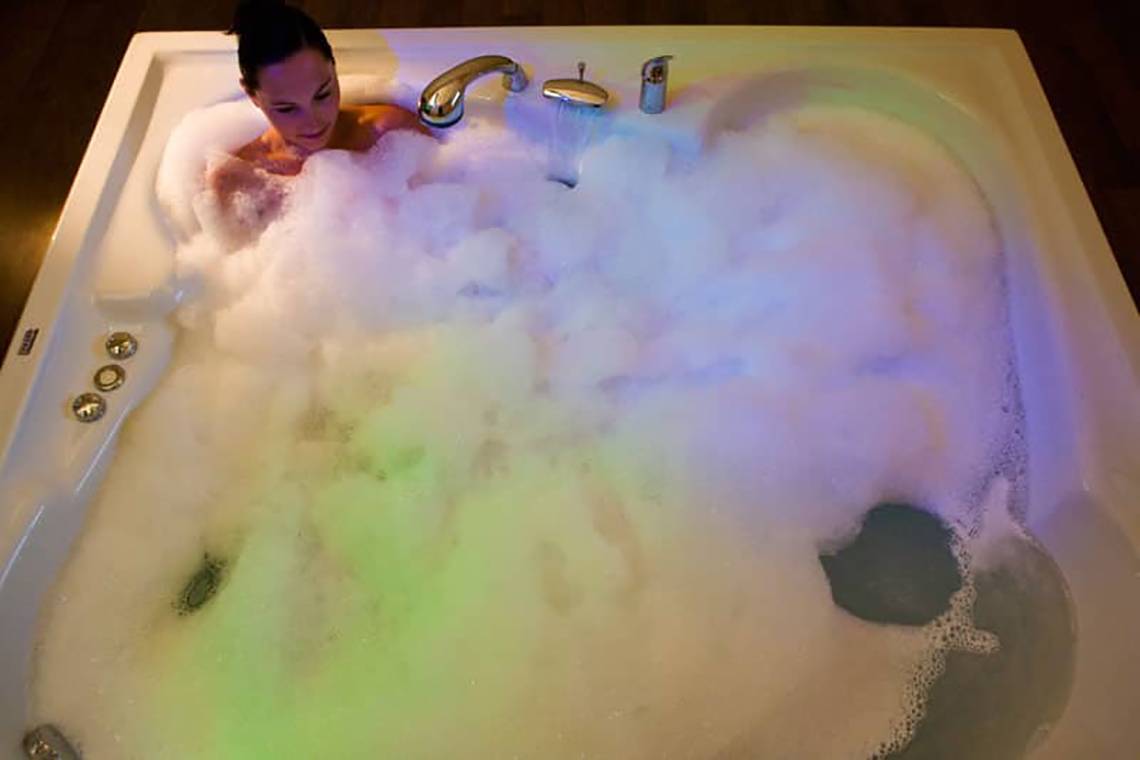 Eine Frau genießt ein Bad in einer weißen Badewanne mit Blasen und Lichteffekten im Fantasia Hotel De Luxe.