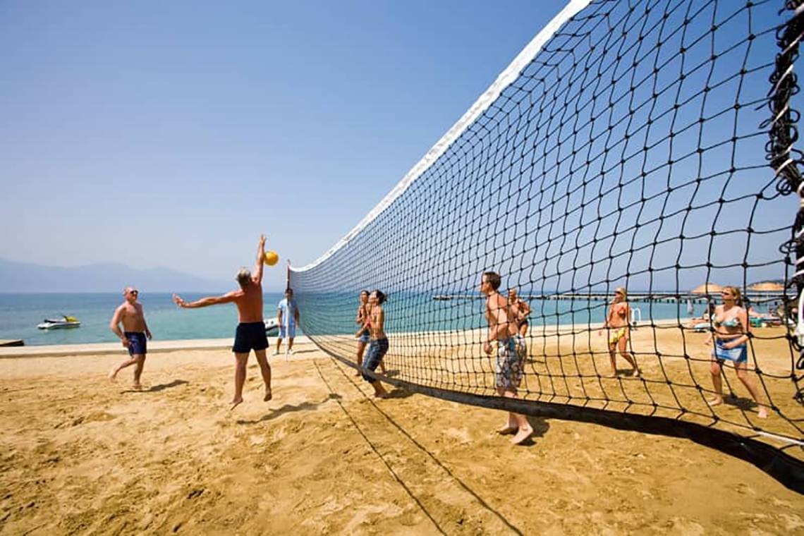 Mehrere Personen spielen Volleyball auf einem Sandstrand mit einem Netz.