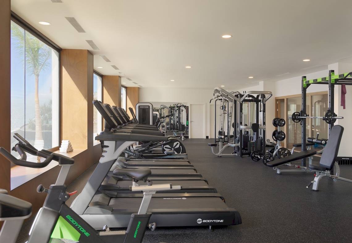 Fitnessstudio im H10 Atlantic Sunset Hotel mit Geräten und Blick auf Palmen.
