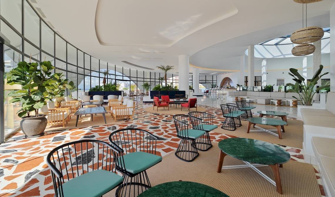 Innenraum des H10 Atlantic Sunset Hotels mit modernen Möbeln, großen Fenstern und grünen Pflanzen.