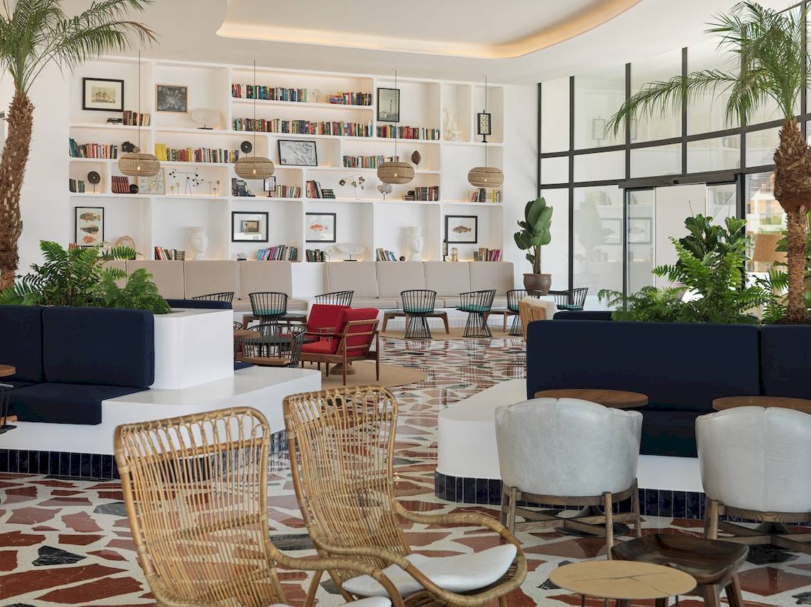 Innenansicht der Lobby des H10 Atlantic Sunset Hotels mit weißen Wänden, Bücherregalen, Pflanzen und verschiedenen Sitzgelegenheiten.
