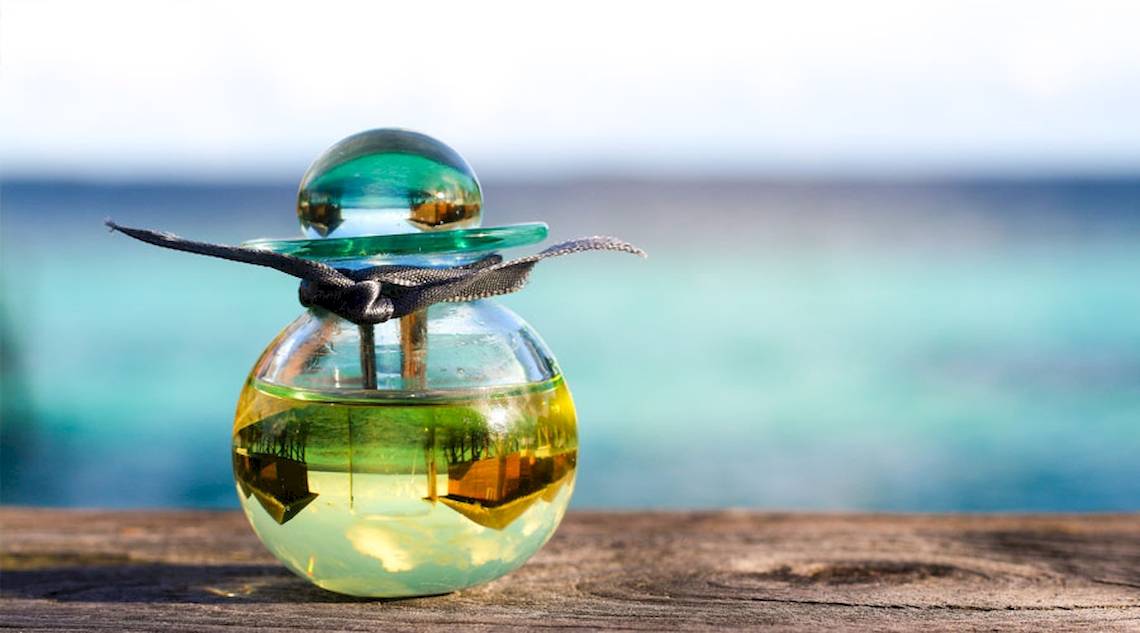 Parfumflasche mit blauem Deckel auf einem Holztisch am Strand des Nova Maldives