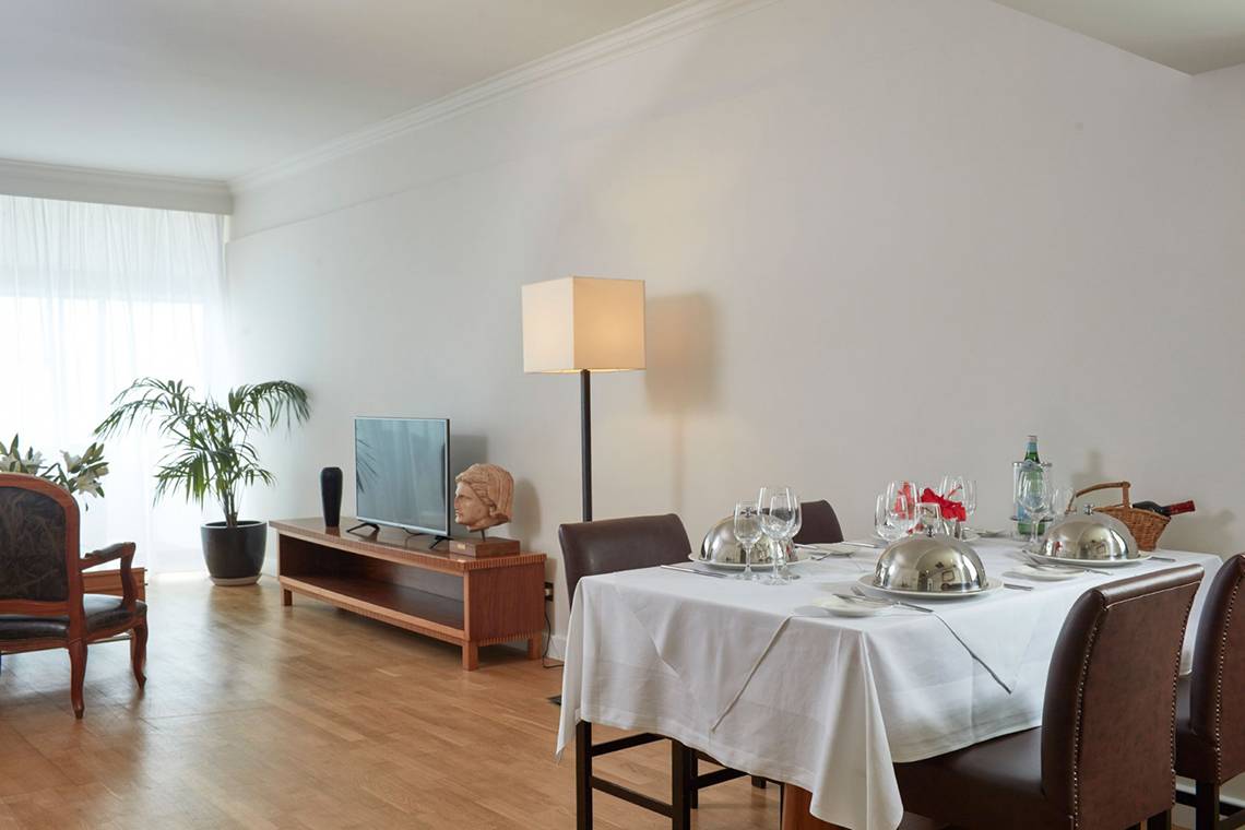 Speisezimmer im Grecian Bay Hotel mit Tisch, Stühlen, Fernseher und Pflanze.